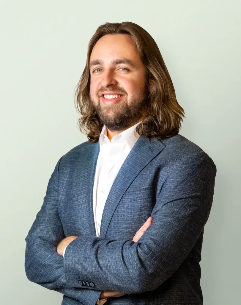 Professional portrait of Paul Walter, CPA, a smiling man with long brown hair and a beard, wearing a dark suit jacket, standing with his arms crossed against a light background.