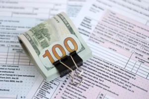 A stack of $100 United States dollar bills held by a binder clip, resting on an official U.S. Individual Income Tax Return Form 1040.