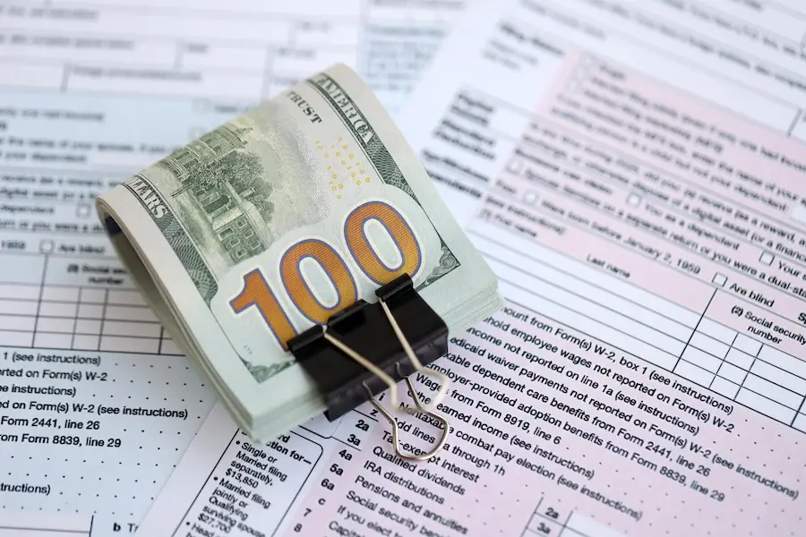 A stack of $100 United States dollar bills held by a binder clip, resting on an official U.S. Individual Income Tax Return Form 1040.